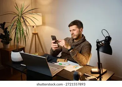 Person using smartphone and laptop at desk workspace