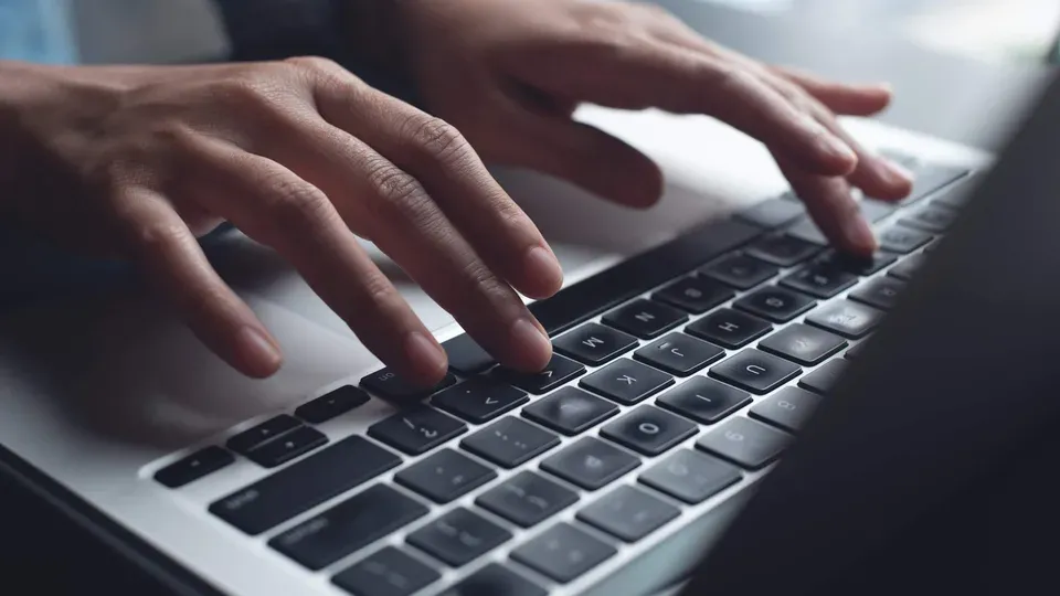 Hands typing on laptop keyboard during work session
