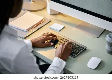 Person working at desk typing on keyboard with notebook